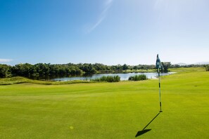 A golf course with a flagstick, water body, and trees. - Indura Beach & Golf Resort, Curio Collection (Tela)