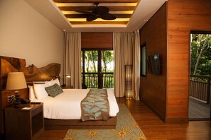 A hotel room with a bed, a nightstand, a lamp, a TV, and a balcony with a view of trees.