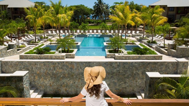 A resort with a central pool, lounge chairs, and palm trees.