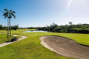 Een golfbaan met een waterpartij, palmbomen en een golfkar.
