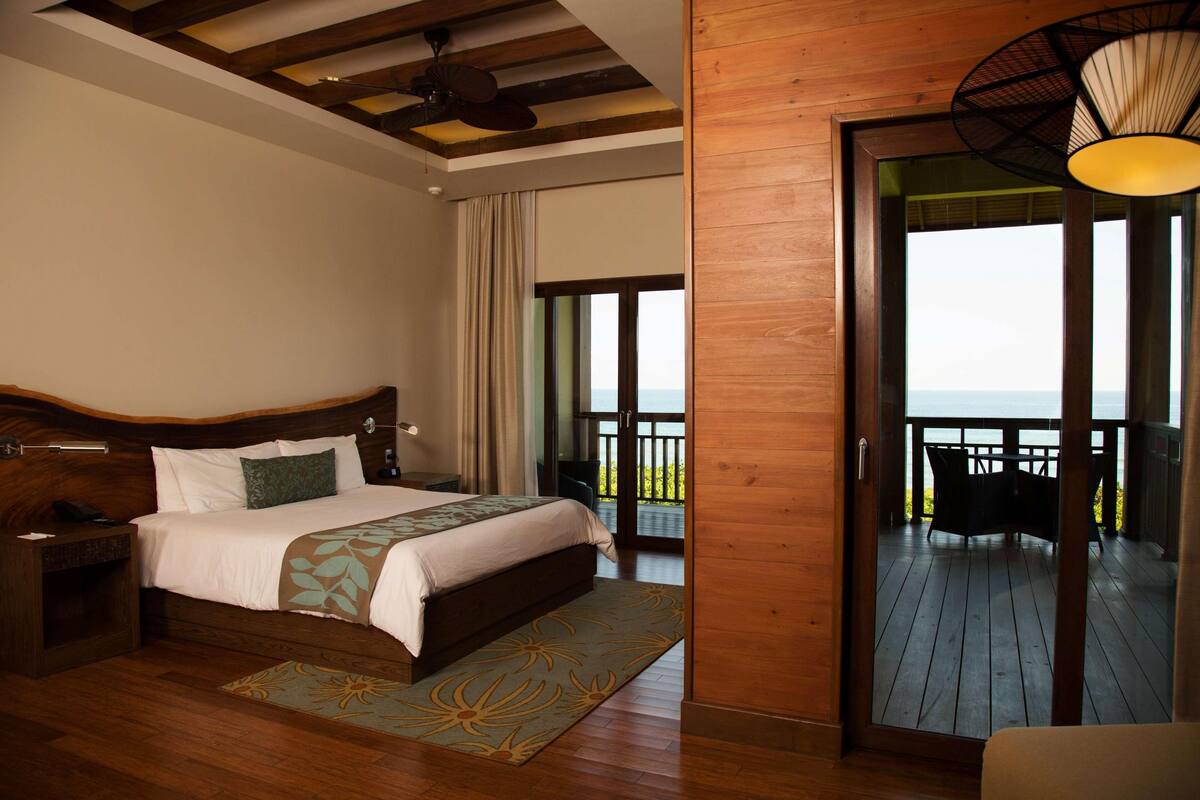 Un dormitorio con techo de madera, una cama grande, una mesita de noche y un balcón con vistas.