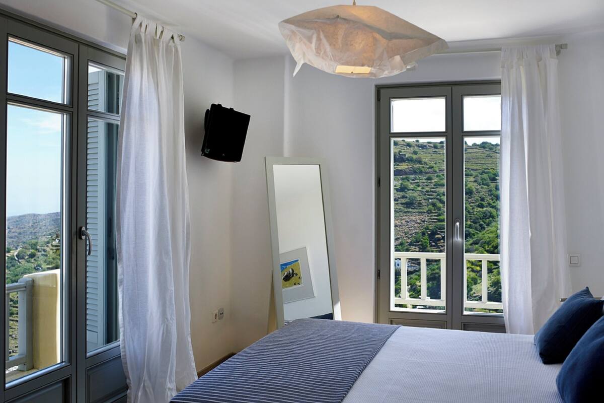Une chambre à coucher comprenant un lit, un luminaire suspendu, un miroir et une vue sur un balcon donnant sur un paysage pittoresque.