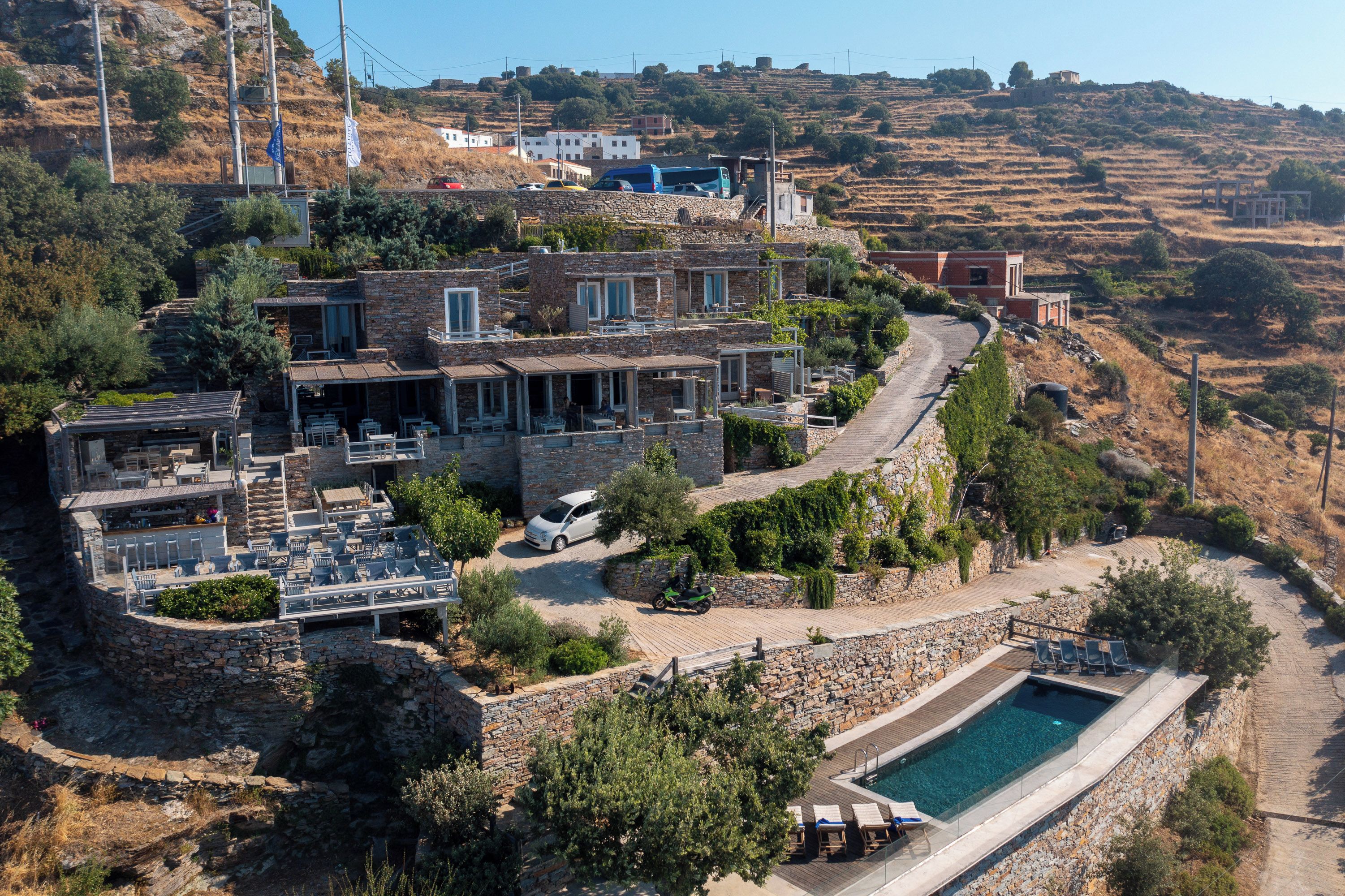 A hillside villa with a swimming pool, outdoor seating, and a winding driveway.