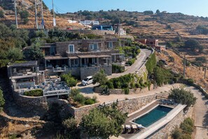 Una villa en la ladera con piscina, mobiliario exterior y un camino de acceso sinuoso.