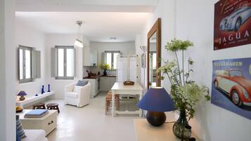 A modern kitchen with white cabinets, a dining area with a white table and chairs, and a living area with a sofa and a small table.