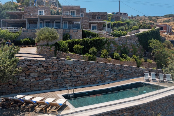 Zona de piscina con paredes de piedra, sillones de descanso y vista despejada de los edificios de la colina circundante.