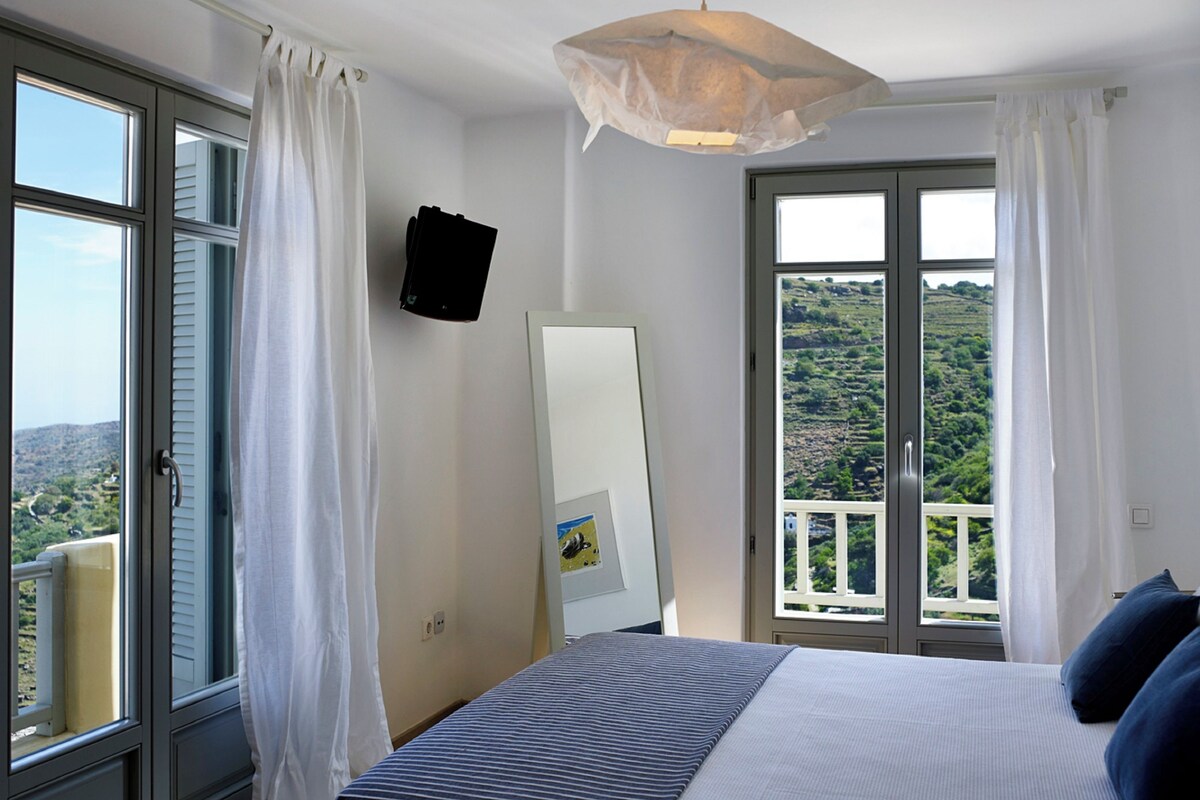Une chambre à coucher comprenant un lit, un luminaire suspendu, un miroir et une vue sur un balcon donnant sur un paysage pittoresque.