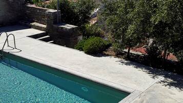 A swimming pool with clear water, wooden lounge chairs, and a view of the sea and hills.