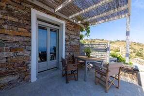 Un edificio de piedra con un patio cubierto, asientos al aire libre y vistas a una colina.