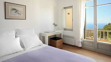 A bedroom with a bed, a bedside table with a vase, a window with a view, and a framed picture on the wall.