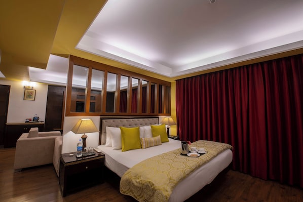 A hotel room with a bed, bedside tables, a desk, a chair, and a large window with curtains. - Citrus Manali Resorts (Manali)
