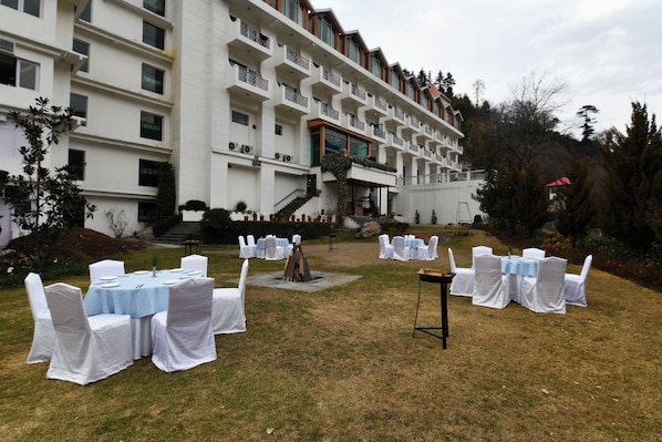 Decoración para boda al aire libre con mesas y sillas, una escalera que lleva a un edificio y una zona con césped y árboles.