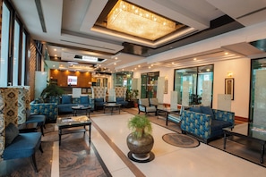 Un hall de hotel con sofás, una mesa de centro, un jarrón decorativo grande y una recepción.