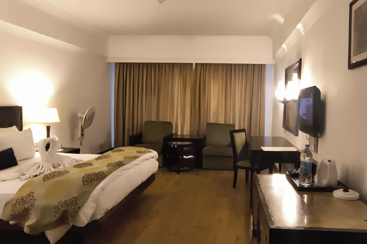 Habitación de hotel con cama, escritorio, silla, televisor y ventana con cortinas.