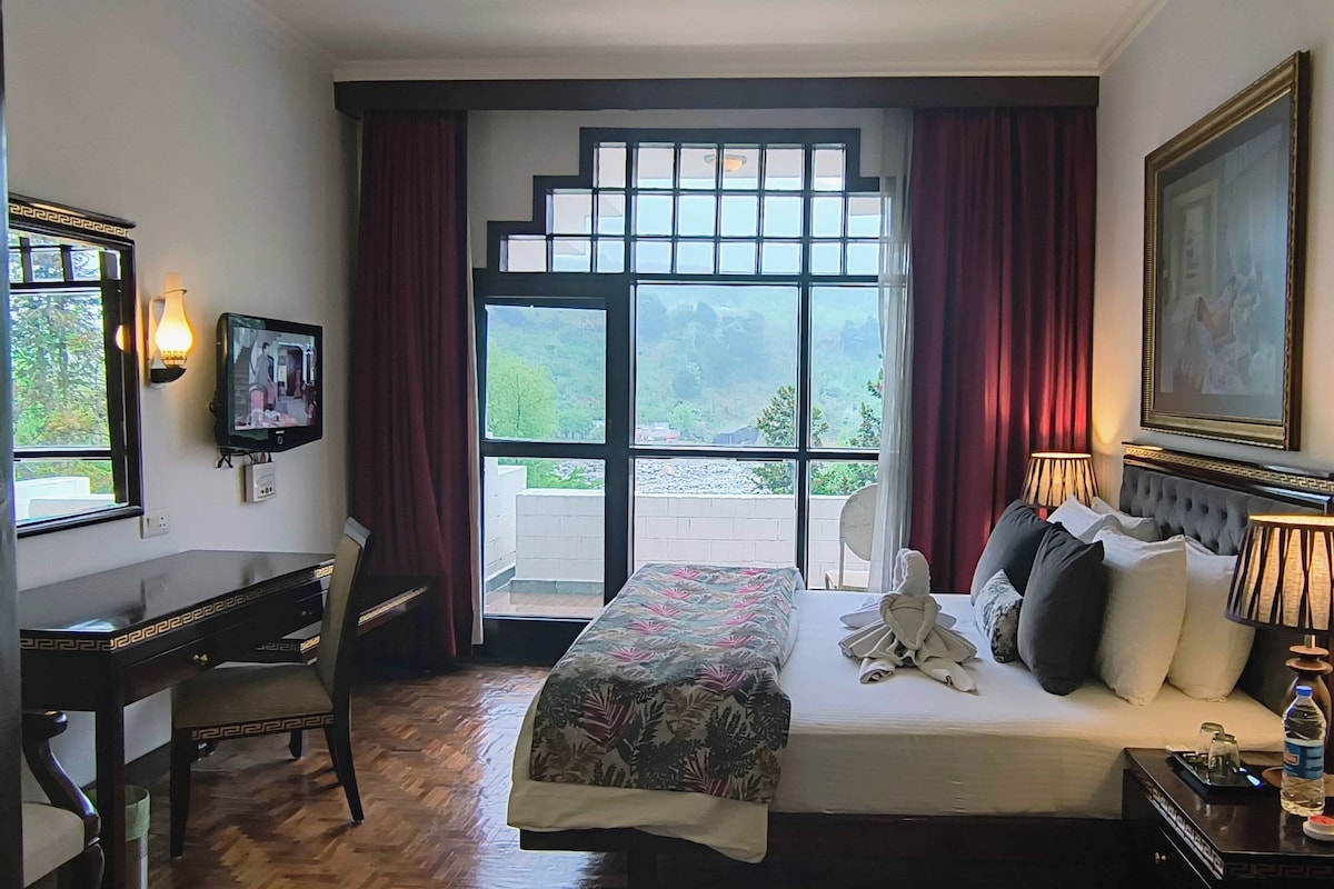 Una habitación de hotel con una cama, un escritorio, un televisor, una ventana con cortinas, un cuadro y una botella de agua sobre la mesita de noche.