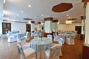A spacious banquet hall with round tables, white chairs with blue sashes, and wooden ceiling accents. - Citrus Manali Resorts (Manali)