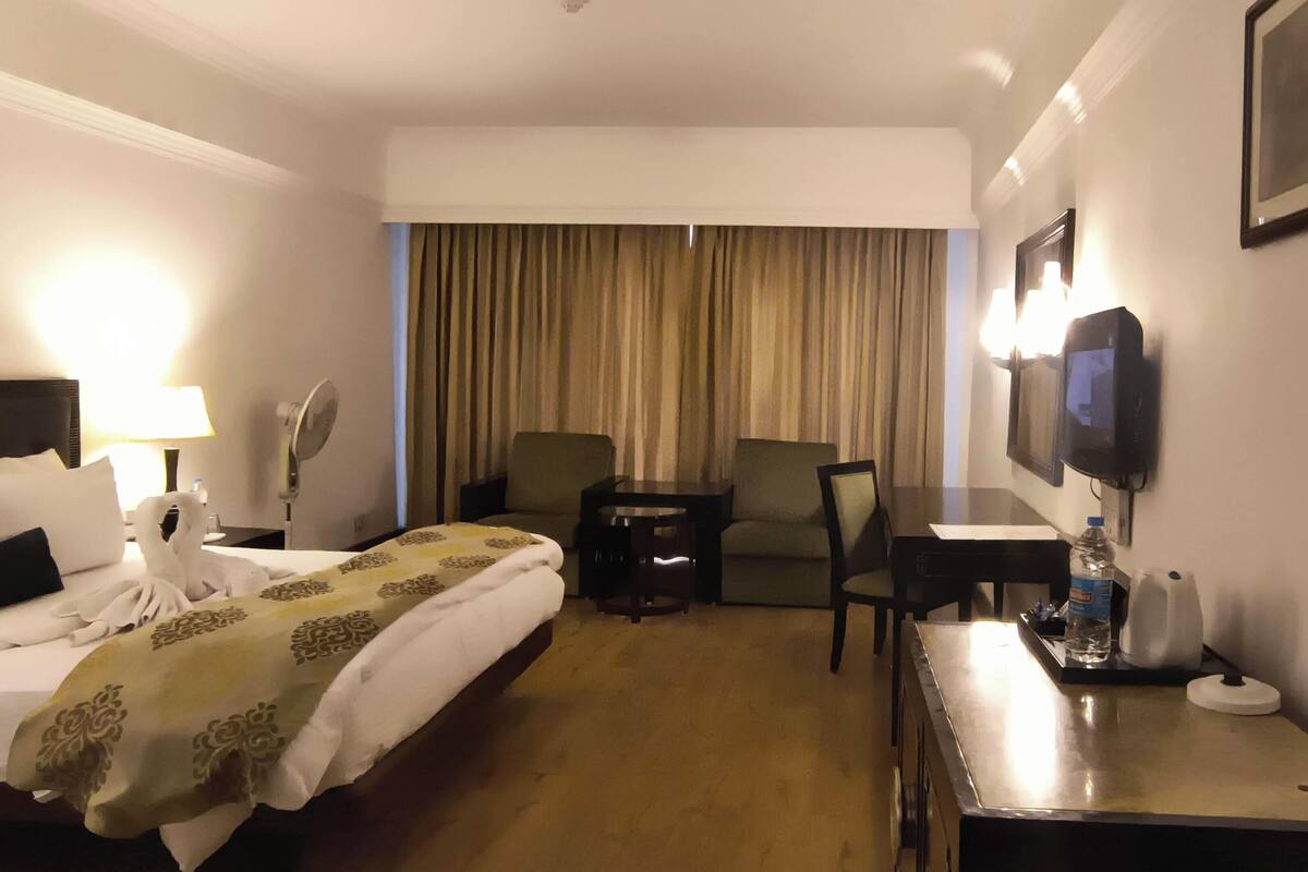 Une chambre d’hôtel équipée d’un lit, d’un bureau, d’une chaise, d’une télévision et d’une fenêtre avec des rideaux.