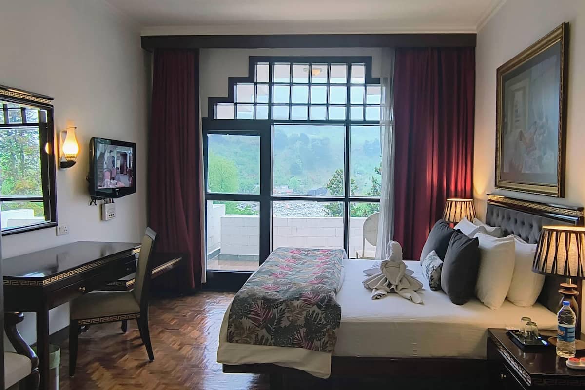Une chambre d’hôtel avec un lit, un bureau, une télévision, une fenêtre avec des rideaux, un tableau et une bouteille d’eau sur la table de chevet.