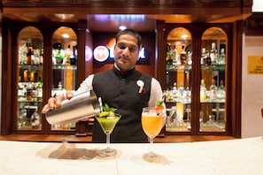 A bartender preparing drinks at a bar with shelves of bottles and glasses in the background. - Citrus Manali Resorts (Manali)