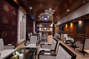 Un vestíbulo de hotel con zona de bar, asientos y una pantalla de televisión.