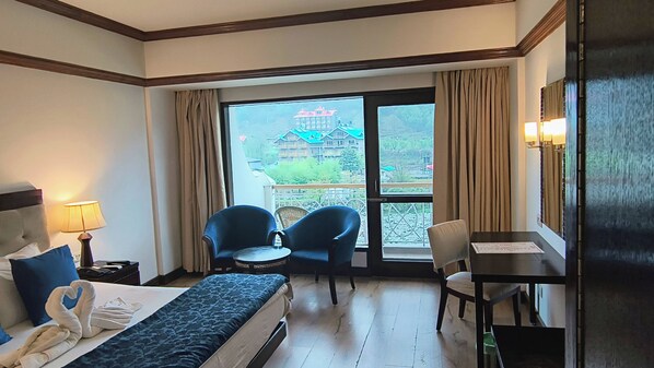 A hotel room with a bed, two chairs, a table, a lamp, and a view of a building through the window. - Citrus Manali Resorts (Manali)