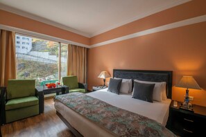 A hotel room with a large bed, two chairs, a desk, a lamp, and a view of a building through the window. - Citrus Manali Resorts (Manali)
