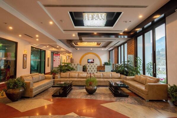 A hotel lobby with a sectional sofa, a large vase, and a television on the wall. - Citrus Manali Resorts (Manali)