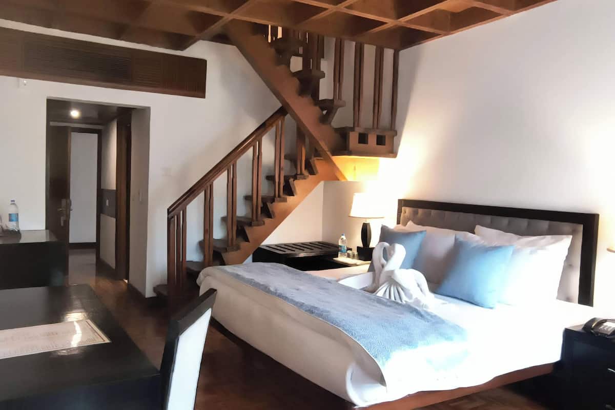 Une chambre d’hôtel avec un lit, un bureau, une chaise, un escalier en bois et une table de chevet avec une lampe.