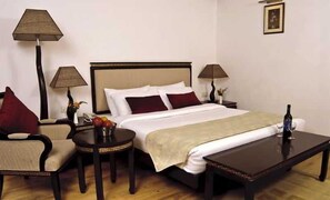 A hotel room with a bed, two bedside tables, a chair, a lamp, and a bottle of wine on a table. - Citrus Manali Resorts (Manali)