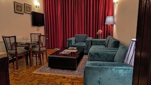 A living room with a sofa, chairs, a coffee table, a TV, and a red curtain. - Citrus Manali Resorts (Manali)