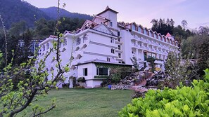 Un hotel de varios pisos con jardín delantero, rodeado de montañas.