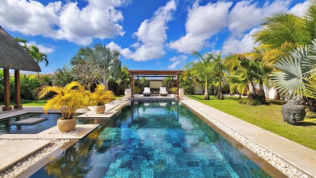 Ein Pool mit einer Pergola und Liegestühlen, umgeben von tropischen Pflanzen und einer Buddha-Statue.
