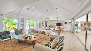 Ein geräumiges Wohnzimmer mit einer großen Couch, einem Couchtisch und einem Essbereich mit weißen Stühlen und einem Tisch.