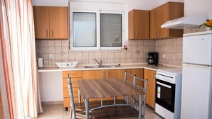 A modern kitchen with wooden cabinets, a stainless steel sink, a dining table with chairs, a coffee maker, and a built-in oven. - Gennadi Garden Apartments (Rhodes)
