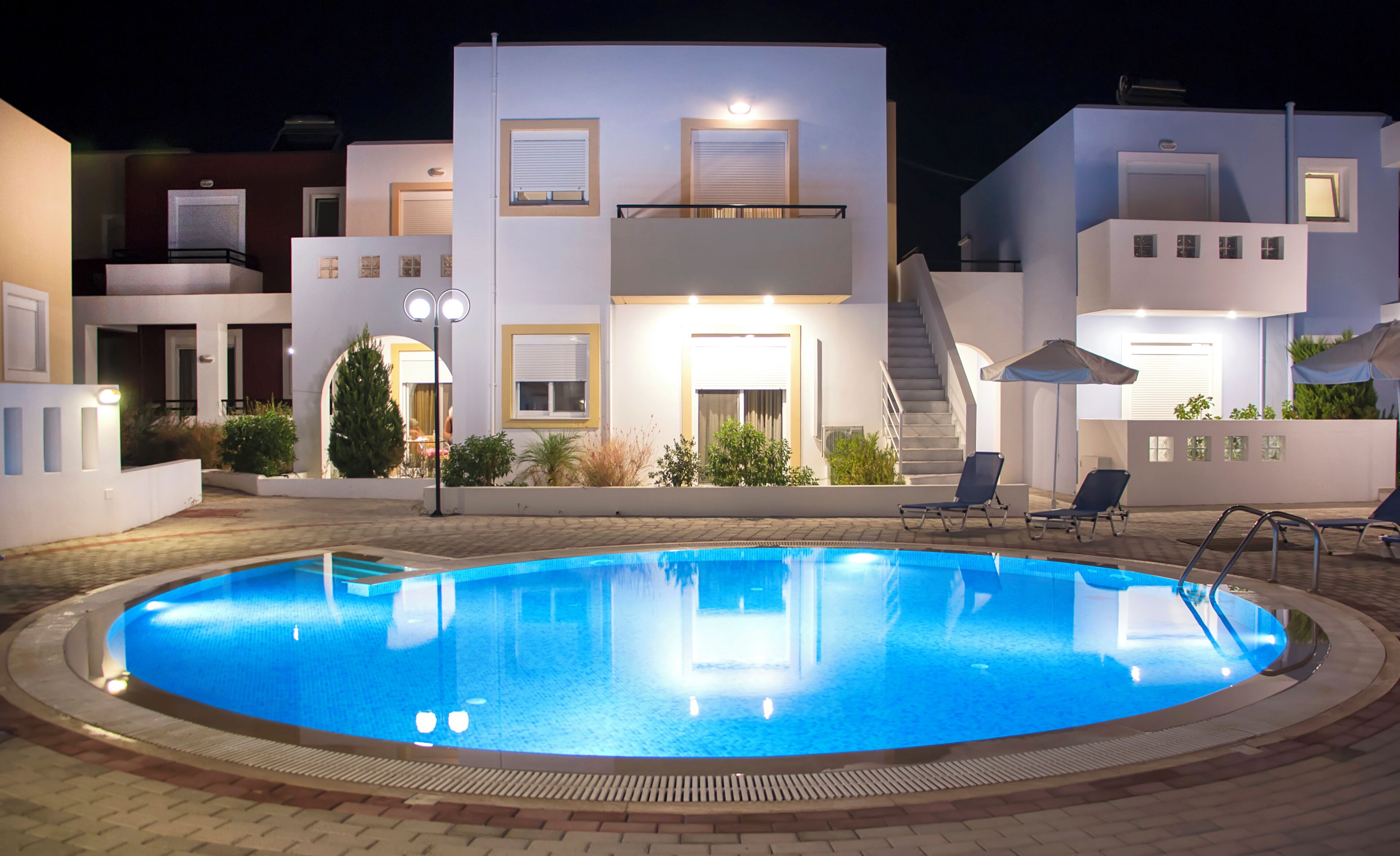 Une piscine à bords nets, entourée d’une zone dallée avec des chaises longues et un escalier menant à un balcon situé au deuxième étage.