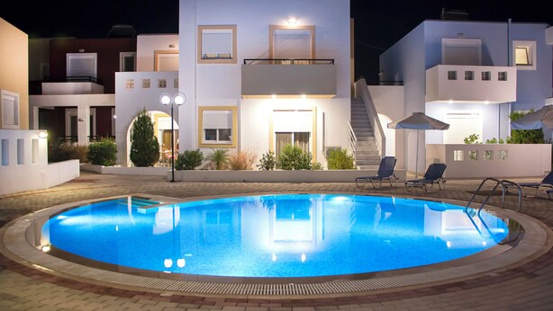 A swimming pool with a clear edge, surrounded by a paved area with lounge chairs and a staircase leading to a second-floor balcony. - Gennadi Garden Apartments (Rhodes)