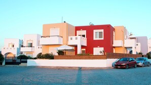 A row of modern, multi-story buildings with balconies, a parking area with several cars, and a clear sky. - Gennadi Garden Apartments (Rhodes)