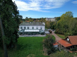 A large white building with a green roof, a covered outdoor seating area, and a well-maintained lawn. - Hotel La Sapiniere (Hallines)