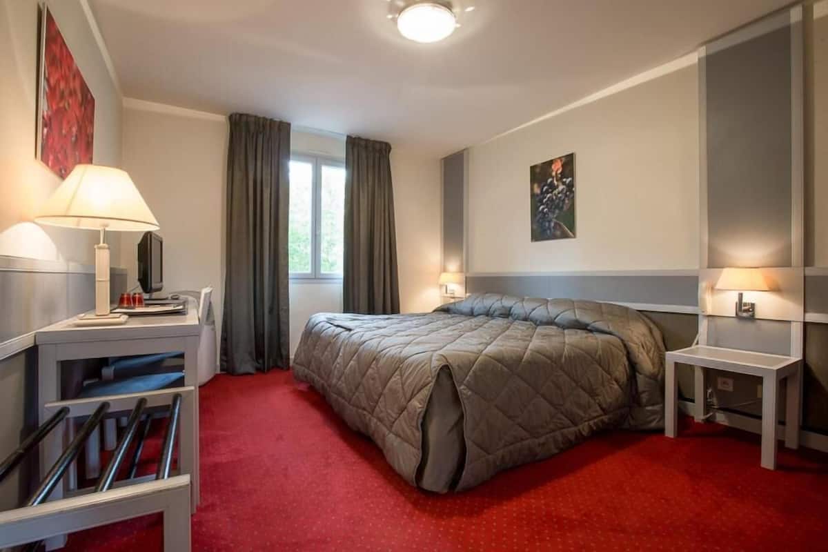 Et hotelværelse med en seng, to sengeborde, et skrivebord, en stol og et vindue med gardiner.