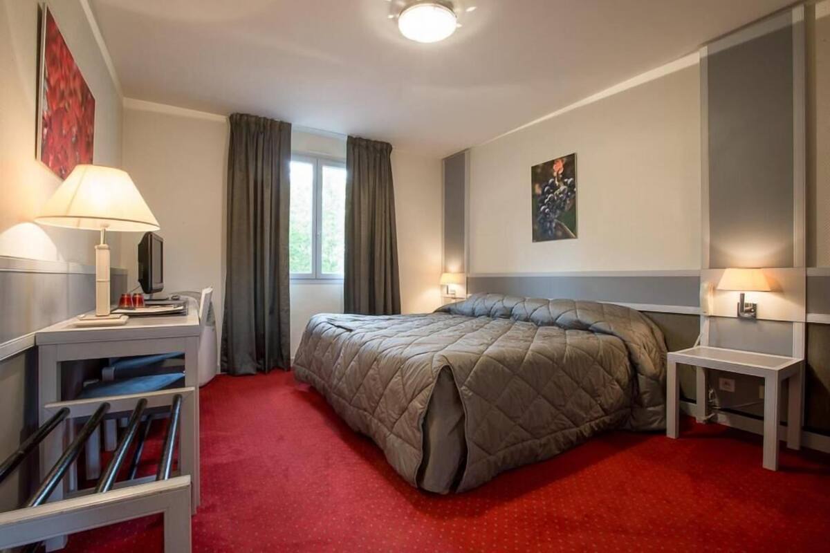 Hotellihuone, jossa on sänky, kaksi yöpöytää, työpöytä, tuoli ja ikkuna, jossa on verhot.