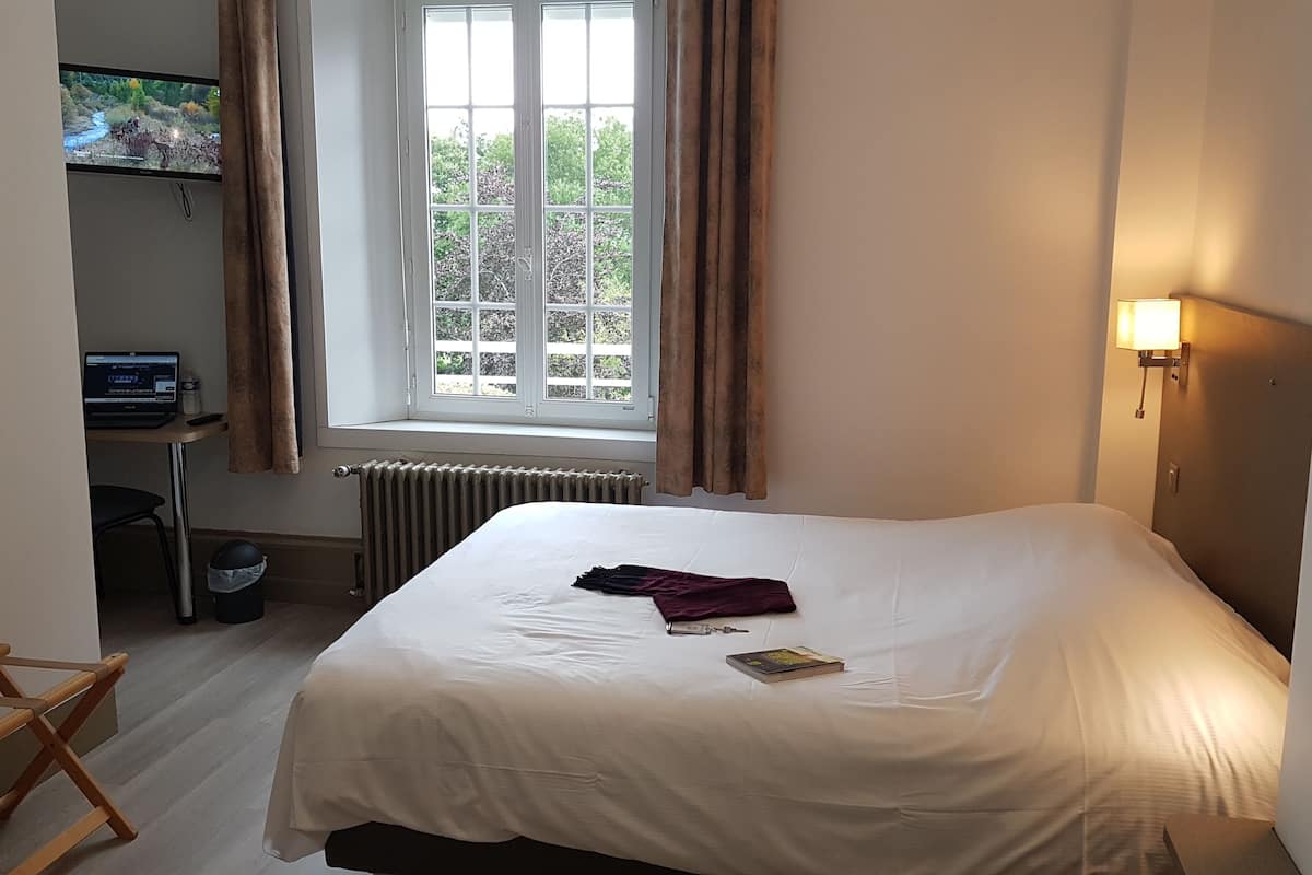Et hotelværelse med en seng, et skrivebord med computer, et vindue med gardiner og en radiator.