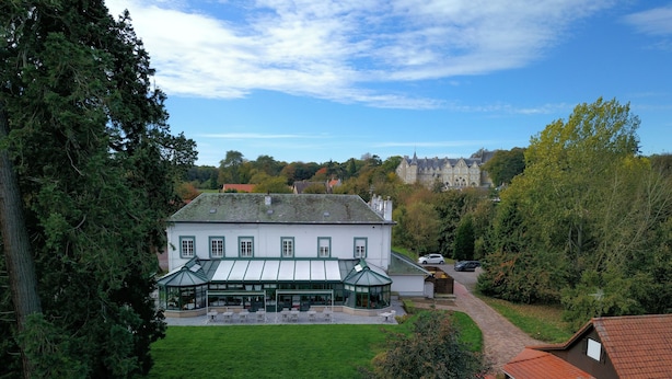 A large white building with a green roof, a covered outdoor seating area, and a well-maintained lawn. - Hotel La Sapiniere (Hallines)