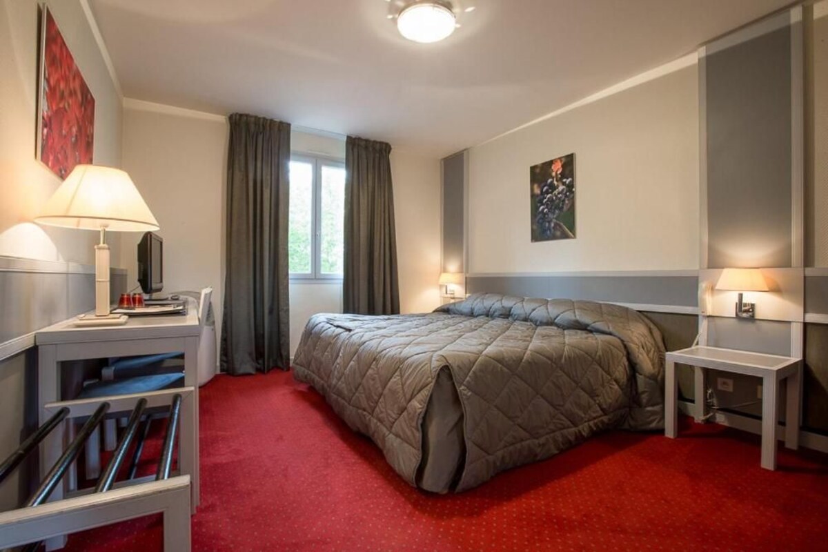 Habitación de hotel con cama, dos mesitas de noche, un escritorio, una silla y una ventana con cortinas.