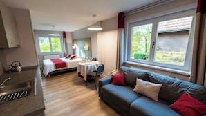 A modern room with a kitchenette, a sofa, a bed, and a dining area. - Hotel La Sapiniere (Hallines)