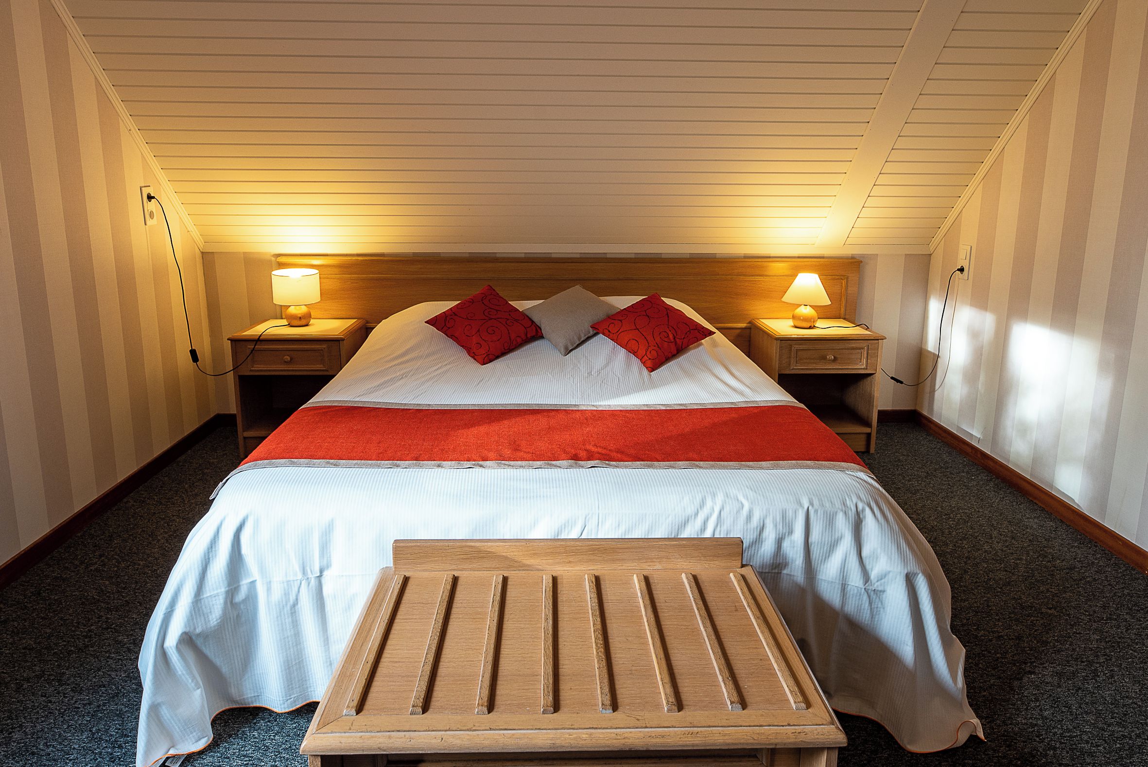 Een hotelkamer met een bed, twee nachtkastjes met lampen, een houten bankje en een vloerbedekking.