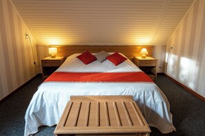 Een hotelkamer met een bed, twee nachtkastjes met lampen, een houten bankje en een vloerbedekking.