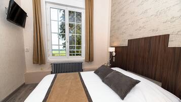 Une chambre d’hôtel avec un lit, une fenêtre, un radiateur et un téléviseur fixé au mur.