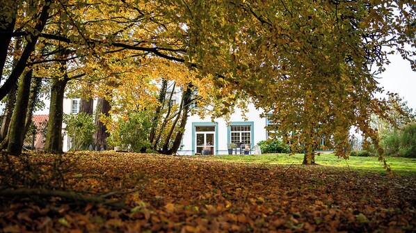 A building with a white facade and blue trim, surrounded by trees with autumn leaves. - Hotel La Sapiniere (Hallines)