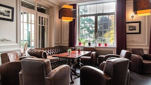 A room with a large window, leather seating, a wooden table, and potted plants. - Hotel La Sapiniere (Hallines)