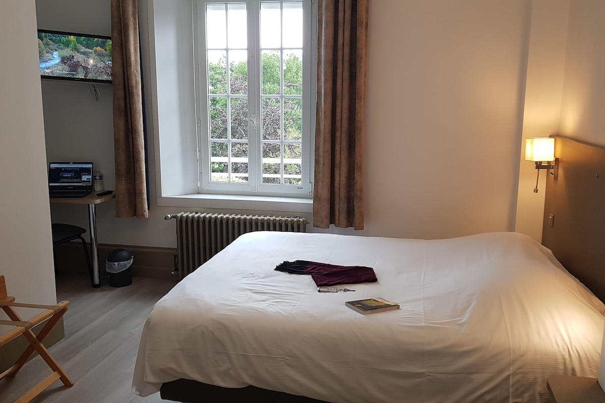 Una habitación de hotel con cama, escritorio con computadora, ventana con cortinas y radiador.